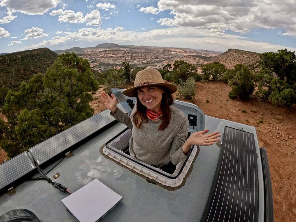 Alaina Hermiston popping through the skylight on the roof of the Rossmonster Baja Trail adventure truck at a free desert campsite with an incredible view